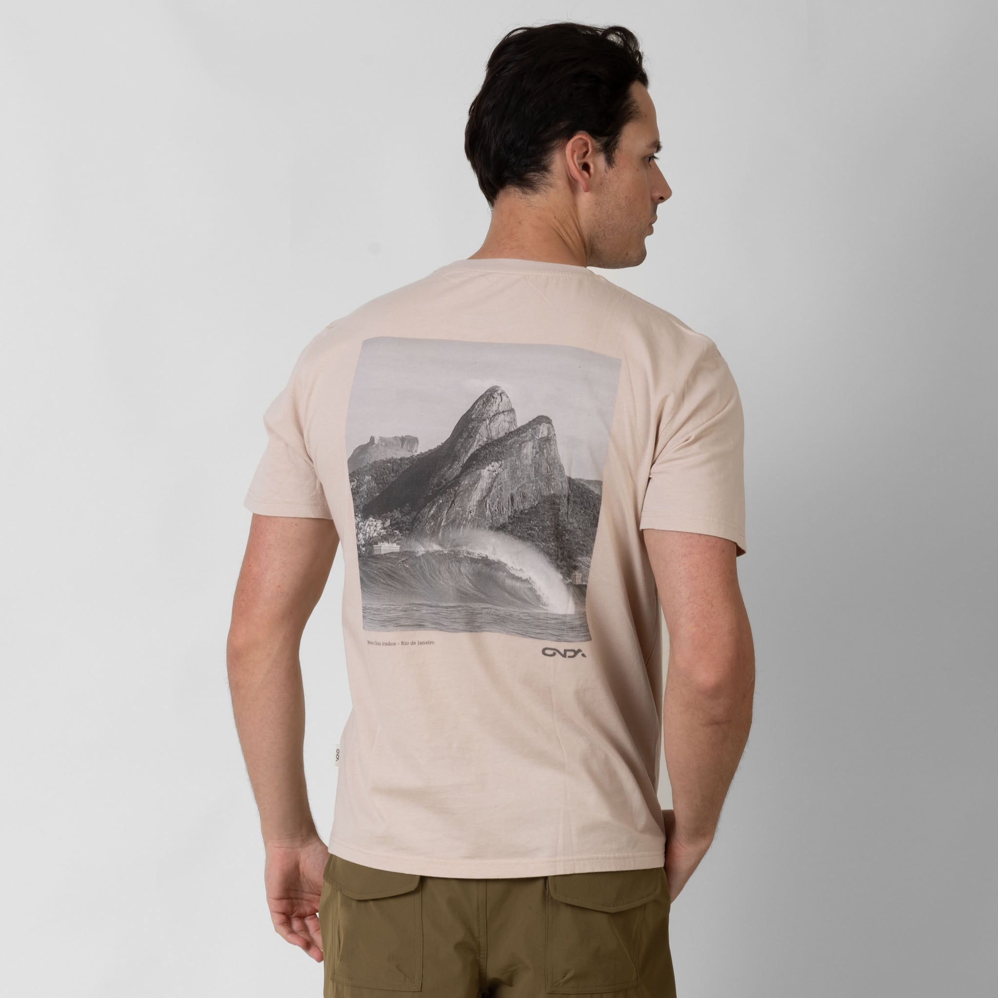 Man wearing a beige t-shirt with a graphic design on the back, standing against a white background