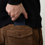 Person wearing brown pants with a pocket, holding a black phone case.