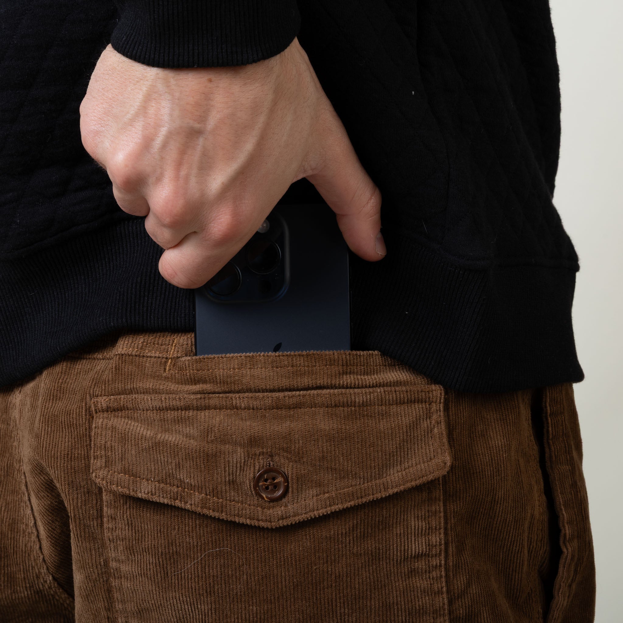 Person wearing brown pants with a pocket, holding a black phone case.
