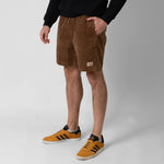 Person wearing brown shorts with onda logo and orange Adidas sneakers on a white background