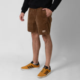 Person wearing brown shorts with onda logo and orange Adidas sneakers on a white background