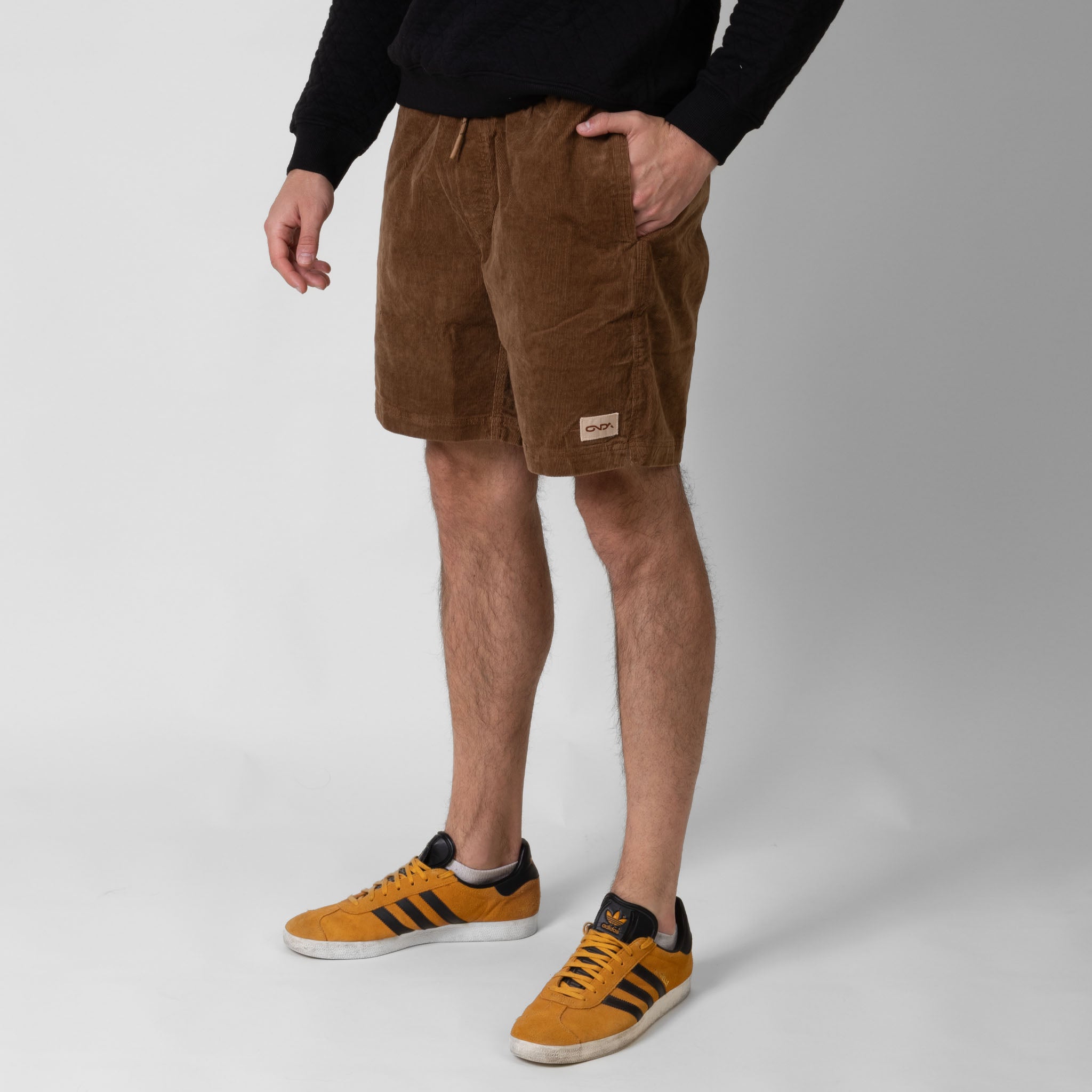 Person wearing brown shorts with onda logo and orange Adidas sneakers on a white background
