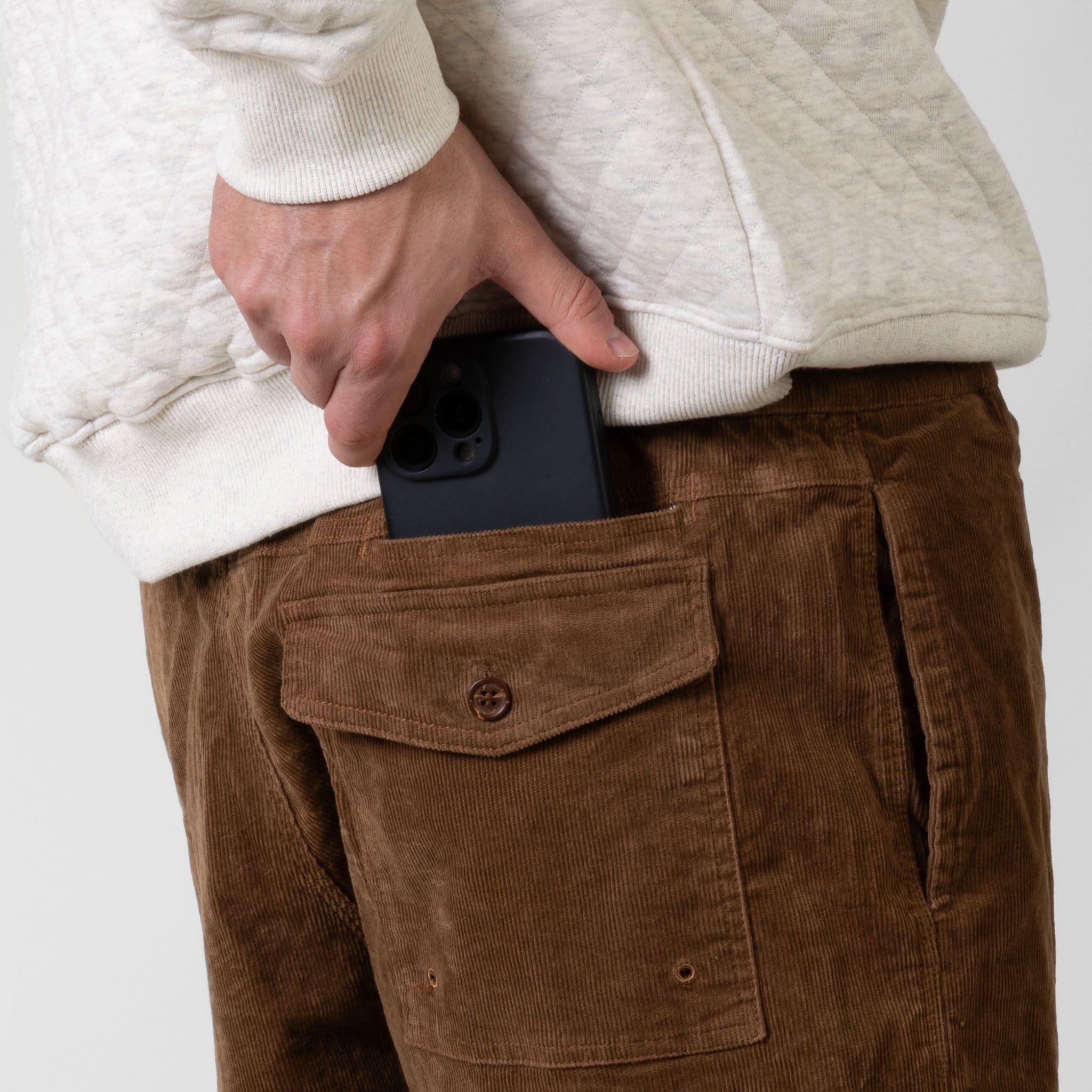 Person wearing brown corduroy pants with a white sweater, holding a black phone in the pocket.