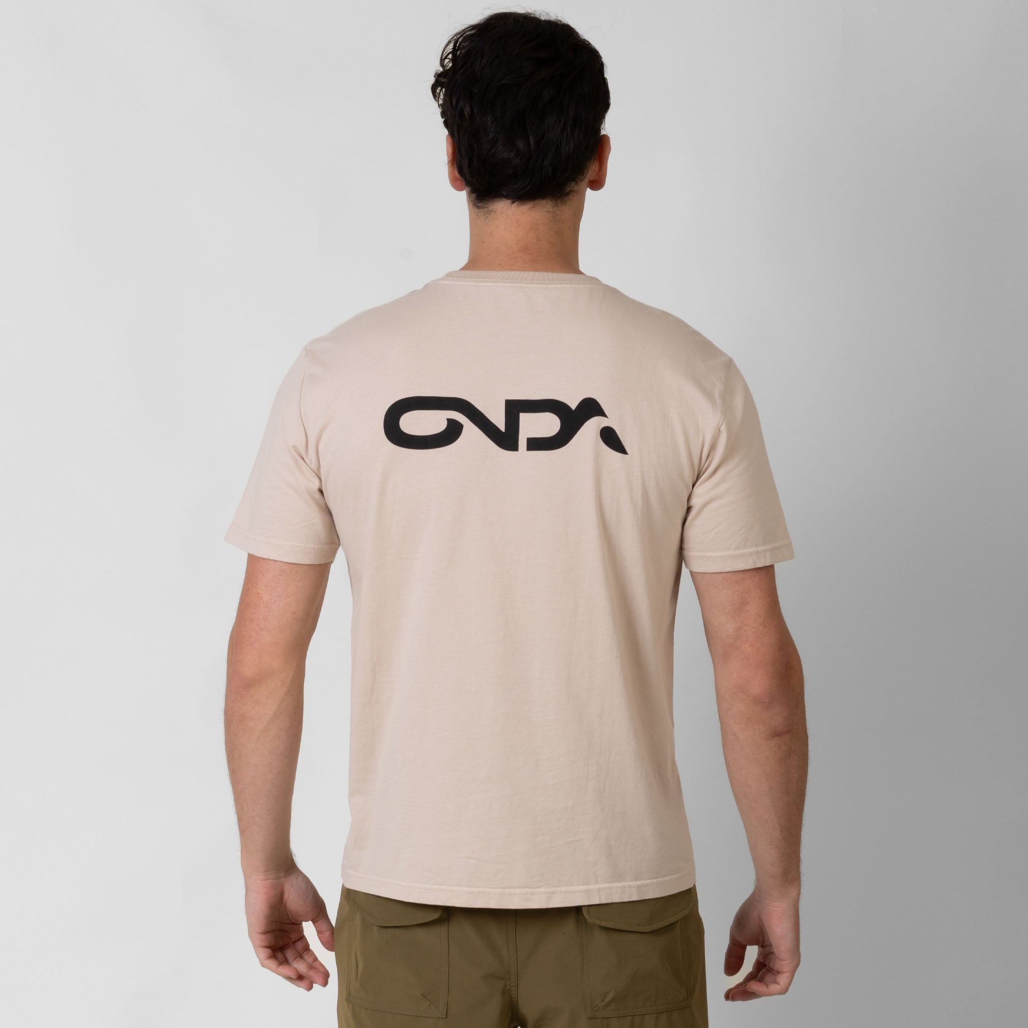 Man wearing a beige t-shirt with a black onda logo on the back against a white background