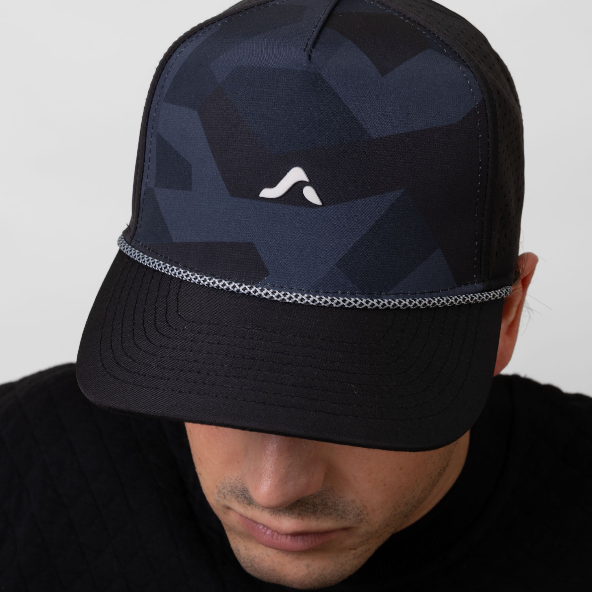 Person wearing a black and navy camouflage cap with a white onda logo on a white background