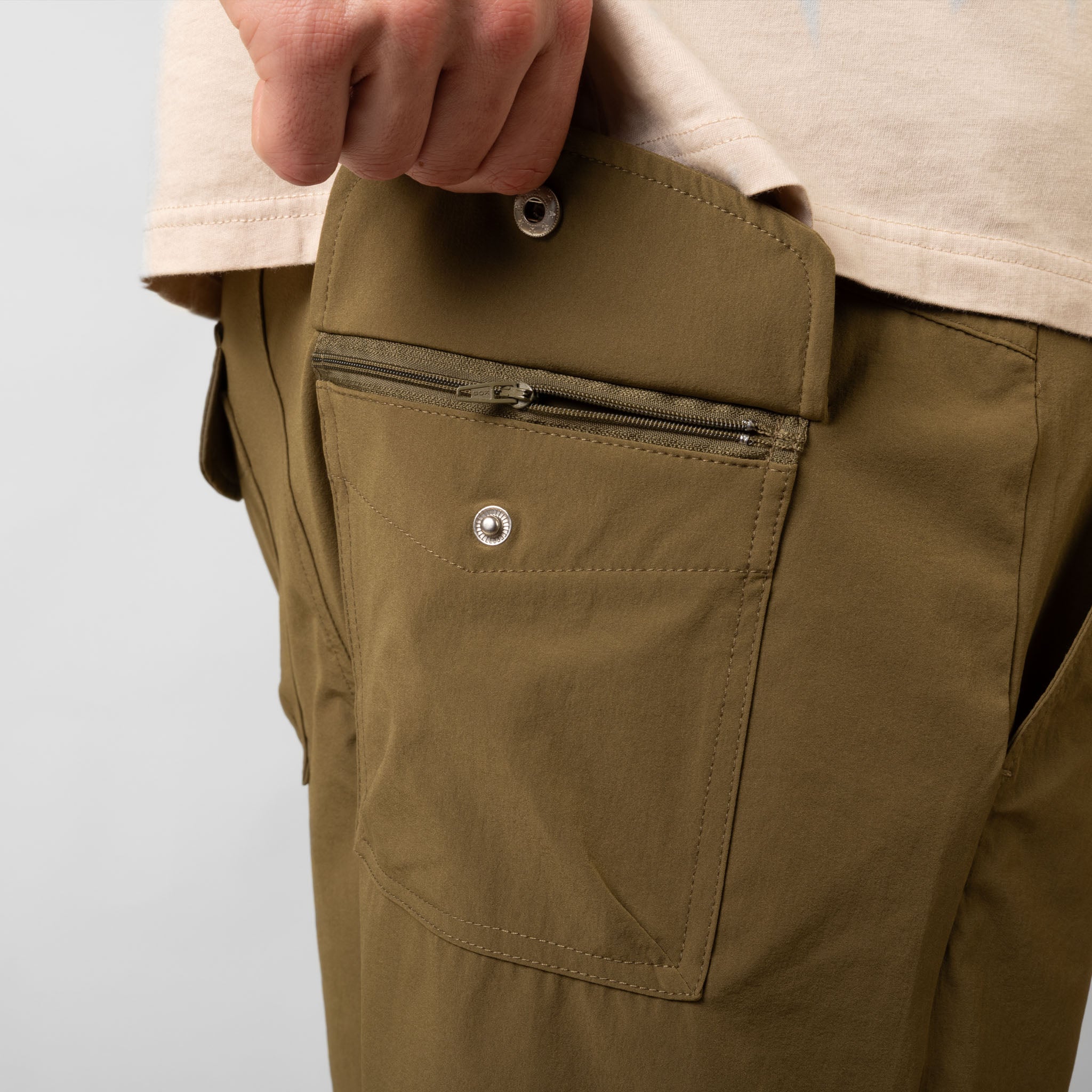 Close-up of a person wearing brown pants with a pocket zipper on a white background