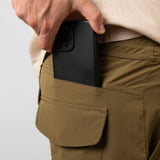 Person placing a black phone case into a pocket of brown pants on a white background
