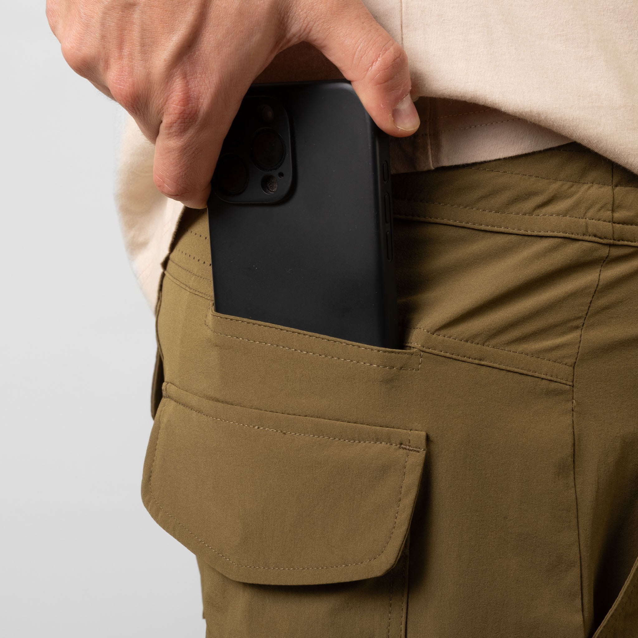 Person placing a black phone case into a pocket of brown pants on a white background