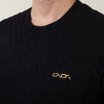 Black sweater with a gold onda logo on a neutral background