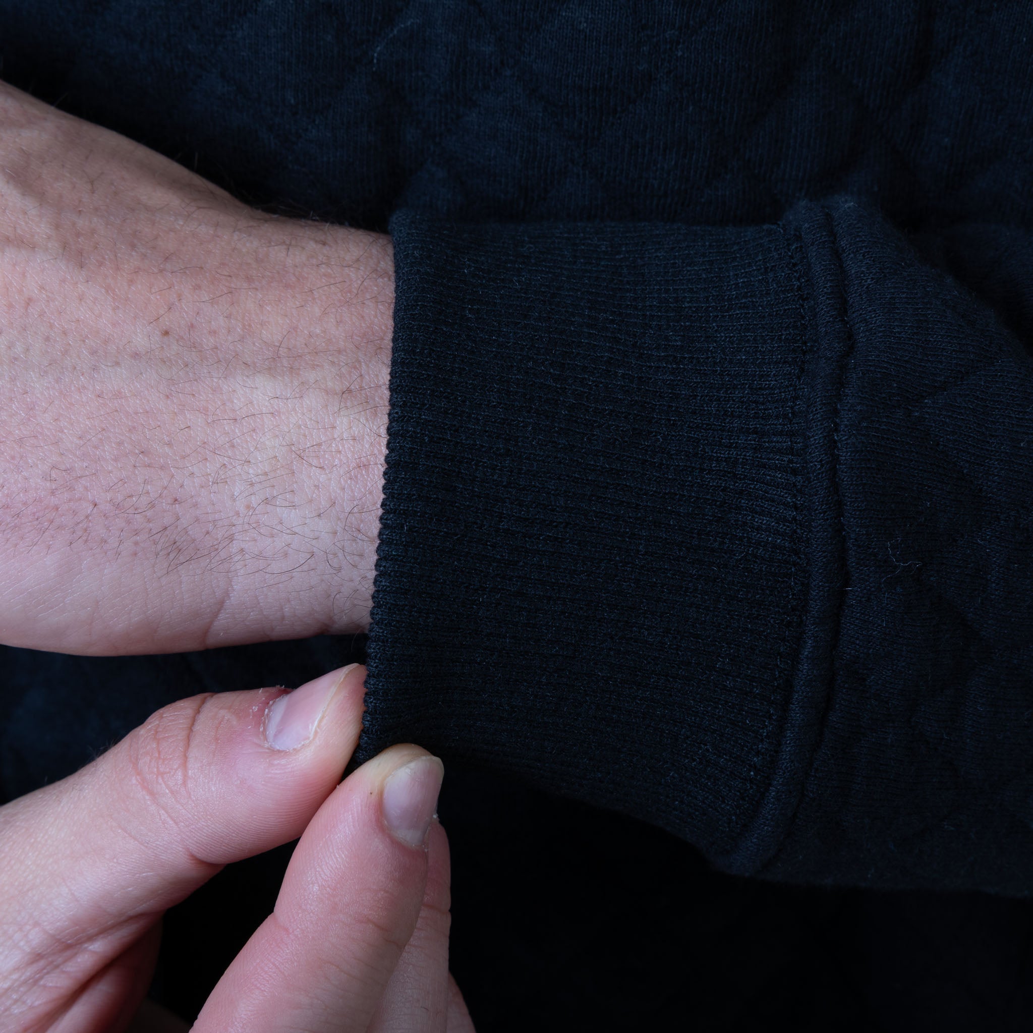 Close-up of a person adjusting the sleeve of a dark sweater.