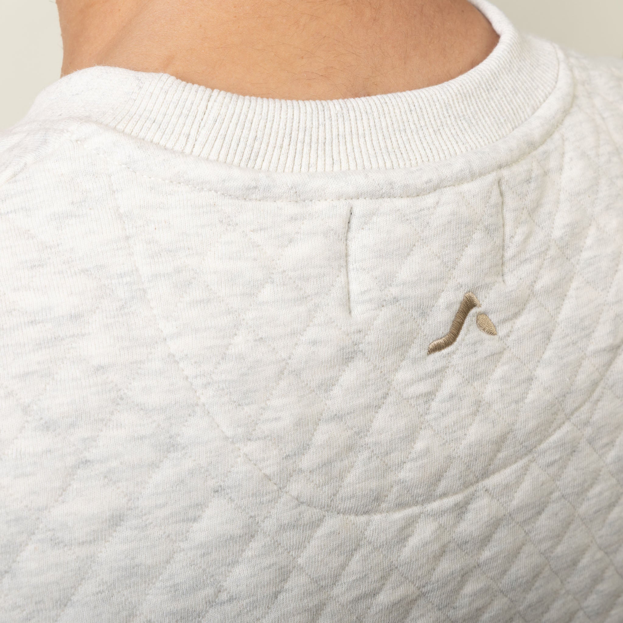 Close-up of a textured white sweater with an onda logo on a neutral background
